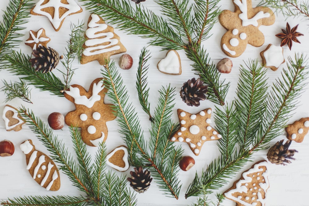 Christmas gingerbread cookies, fir branches and pine cones composition on wooden background flat lay. Tasty homemade gingerbread tree, reindeer, star cookies. Happy Holidays!