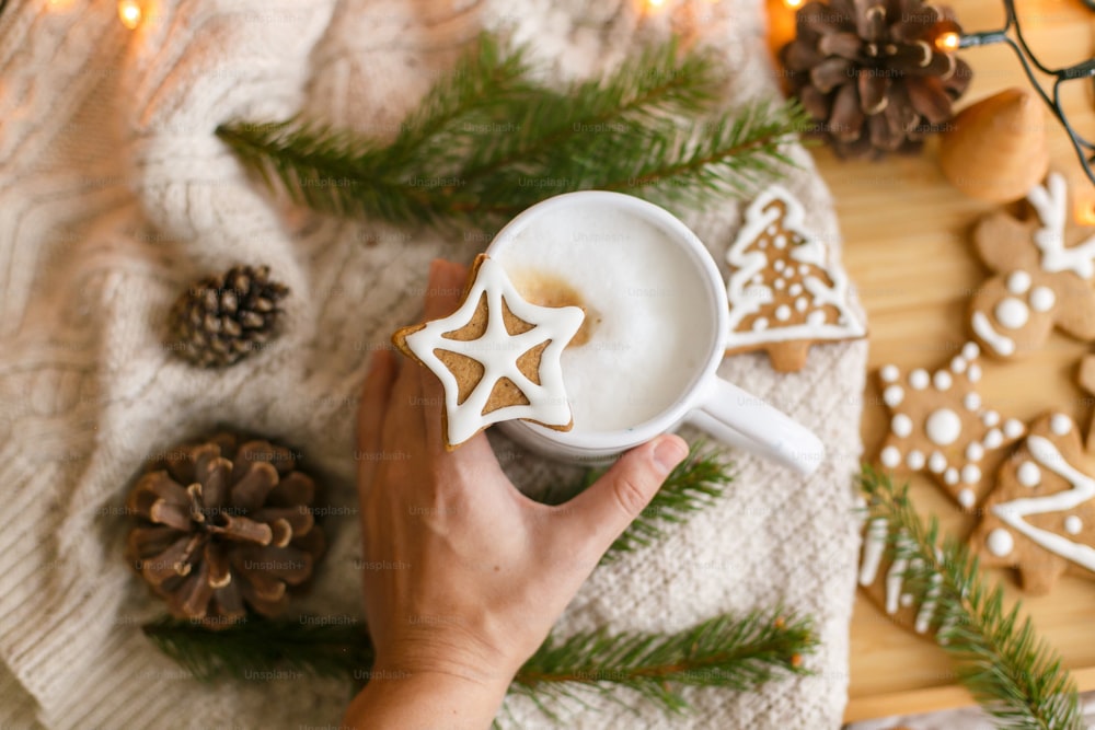 Hand holding warm coffee with christmas star gingerbread cookie on background of cozy knitted sweater. Hello winter, top view. Merry Christmas and Happy Holidays!