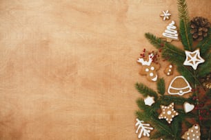 Biscuits de Noël en pain d’épices et branches de sapin bordent sur fond en bois. Carte de vœux de saison à plat avec de l’espace pour le texte. Joyeux Noël et Joyeuses Fêtes !