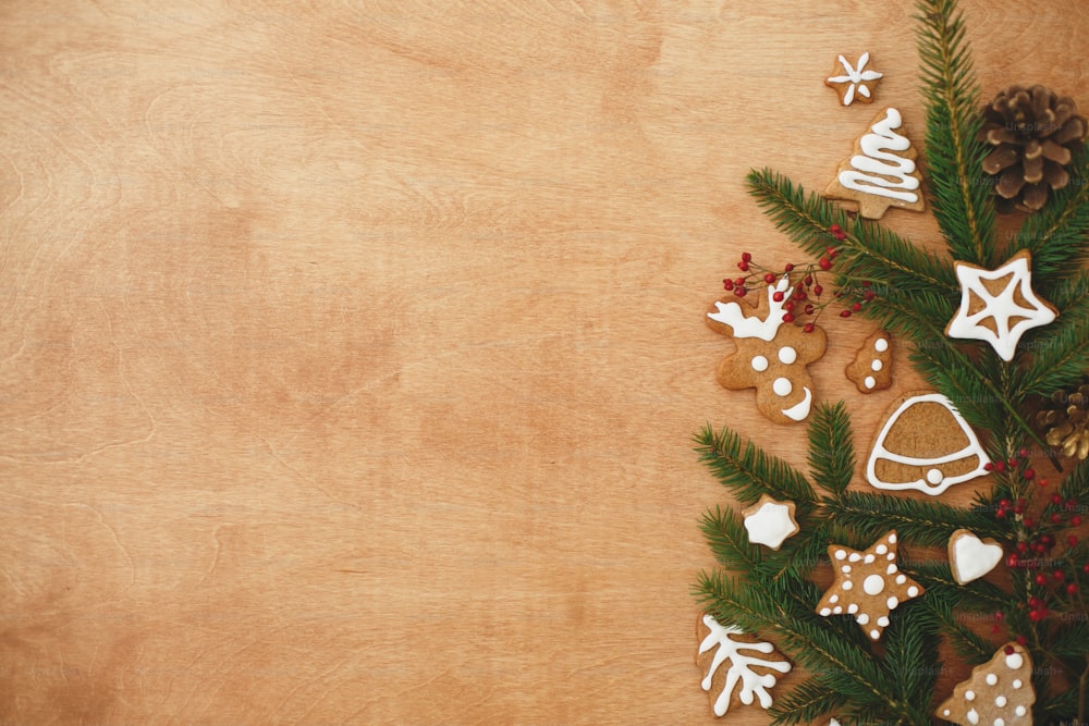 Christmas gingerbread cookies and fir branches border on  wooden background. Season's greeting card flat lay with space for text. Merry Christmas and Happy Holidays!