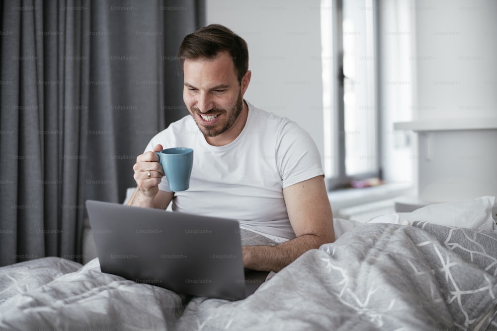 Young man watching movie in bed. Handsome man enjoying in morning.