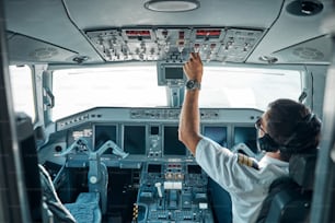 Un joven piloto con uniforme y artilugios está sentado en el control de la cabina y usa conmutadores para volar aviones