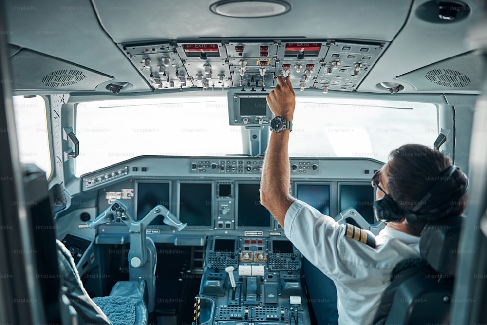 Il giovane pilota in uniforme e gadget è seduto al controllo nella cabina di pilotaggio e utilizza gli switcher per l'aereo di volo