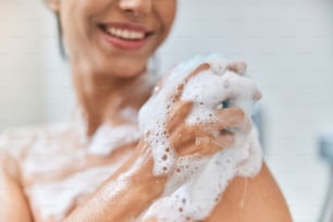 집에서 샤워를 하는 손에 거품이 많은 수건을 들고 웃고 있는 여인의 클로즈업