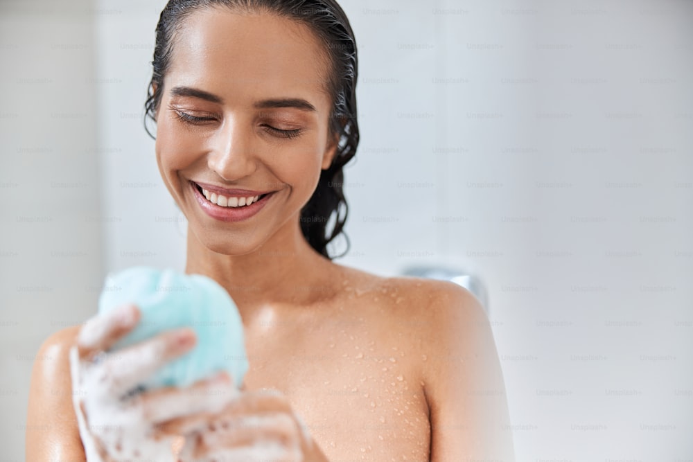 Beautiful smiling lady with exfoliating washcloth in her hand taking shower at home