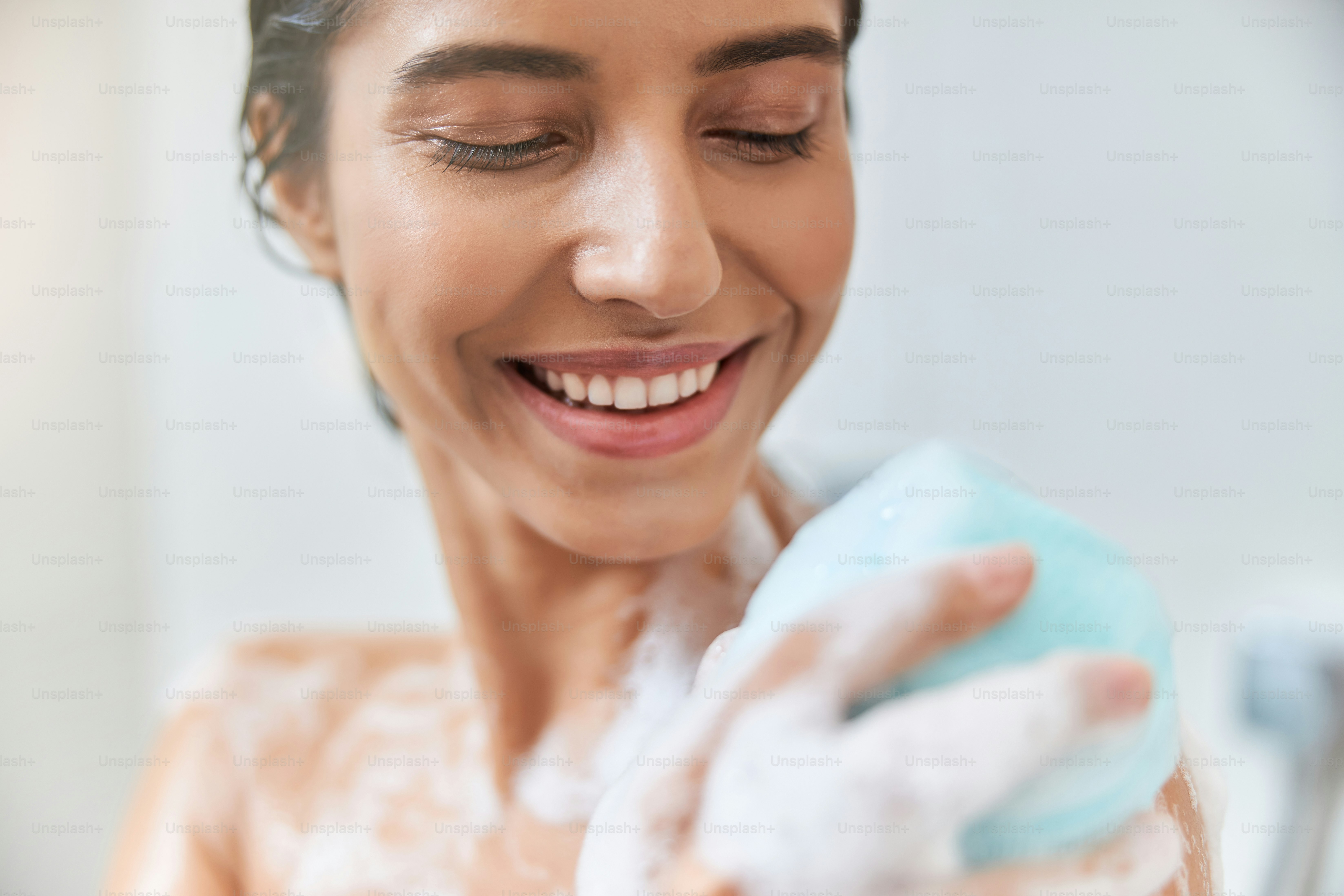Close up of smiling pretty lady using exfoliating bath sponge while