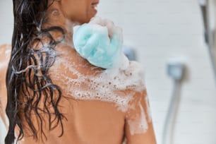 Primer plano de una dama con el cabello mojado usando una esponja de baño exfoliante mientras se ducha en casa