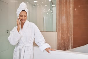 Beautiful smiling lady in white bathrobe having phone conversation in spa salon