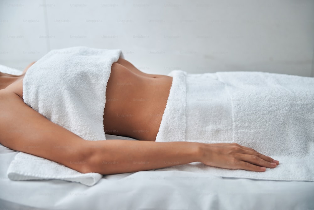 Close up of female body with towel on breast lying on daybed with white sheets