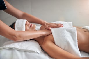 Charmante jeune femme avec un tissu blanc sur les yeux allongée sur une table de massage tout en recevant un massage professionnel