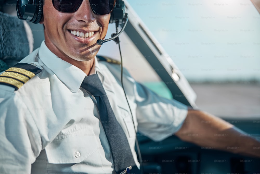 Verkürztes Kopfporträt eines fröhlichen, gutaussehenden Mannes mit professionellen Kopfhörern, der am Steuer im Cockpit sitzt
