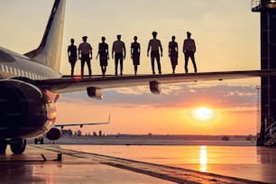 Close up image of unrecognizable aviation team in uniform standing on the wing of big passenger airplane in the outdoors