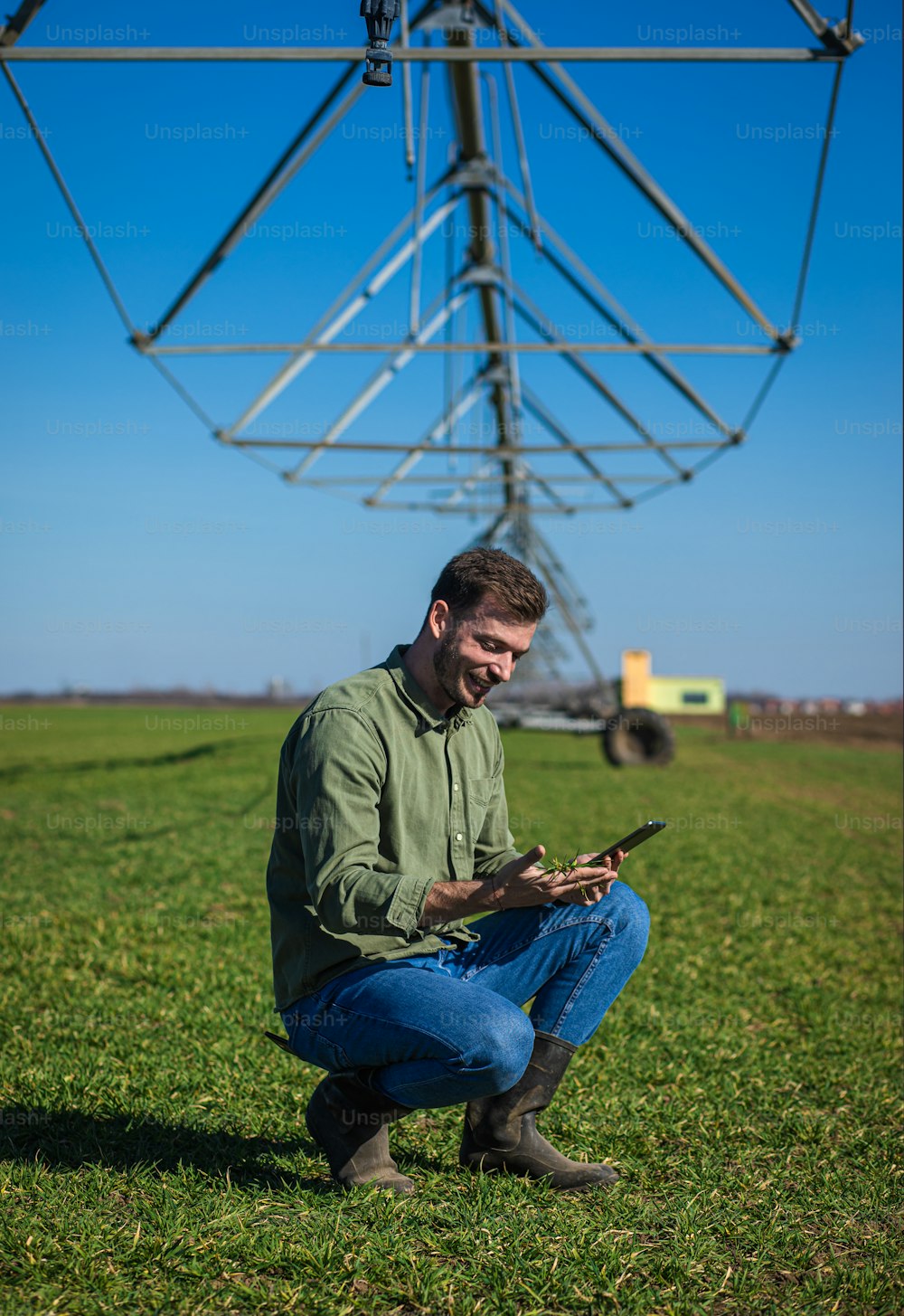 젊은 농부는 밀밭에 서서 태블릿에 관개 시스템을 설치합니다.