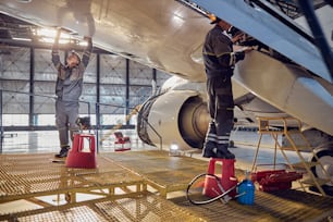 Ritratto a figura intera di vista laterale di meccanici dell'aviazione degli uomini che riparano e controllano lo spoiler e i flap sull'aereo
