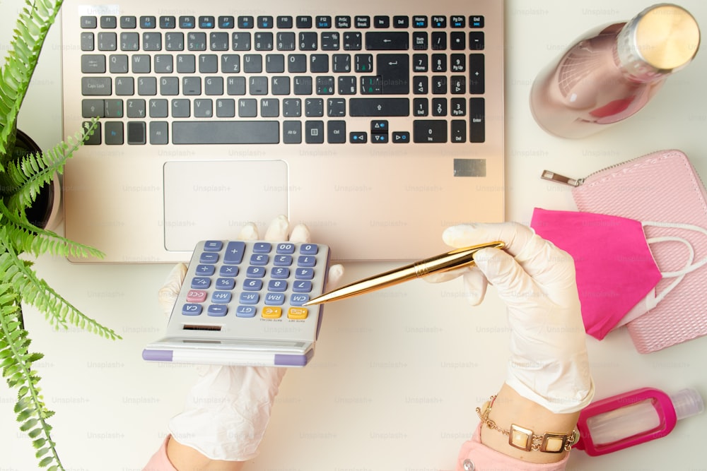 Upper view of female in white rubber gloves talking video call near medical mask, sanitiser and wallet on white table.