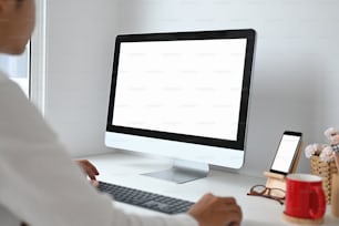 Foto recortada de un joven que trabaja con una computadora y un teléfono inteligente con pantalla blanca en el espacio de trabajo.