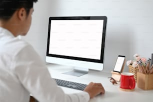 Ausschnittaufnahme eines jungen Mannes, der sein Projekt auf einem Computer-PC mit weißem Bildschirm auf weißem Schreibtisch plant.