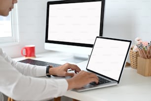 Foto recortada de manos escribiendo en una computadora portátil con pantalla en blanco en el espacio de trabajo.