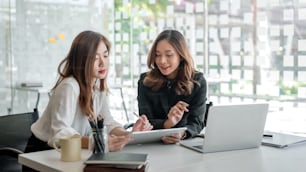 Two young beautiful asian business woman in the conversation, exchanging ideas at work.