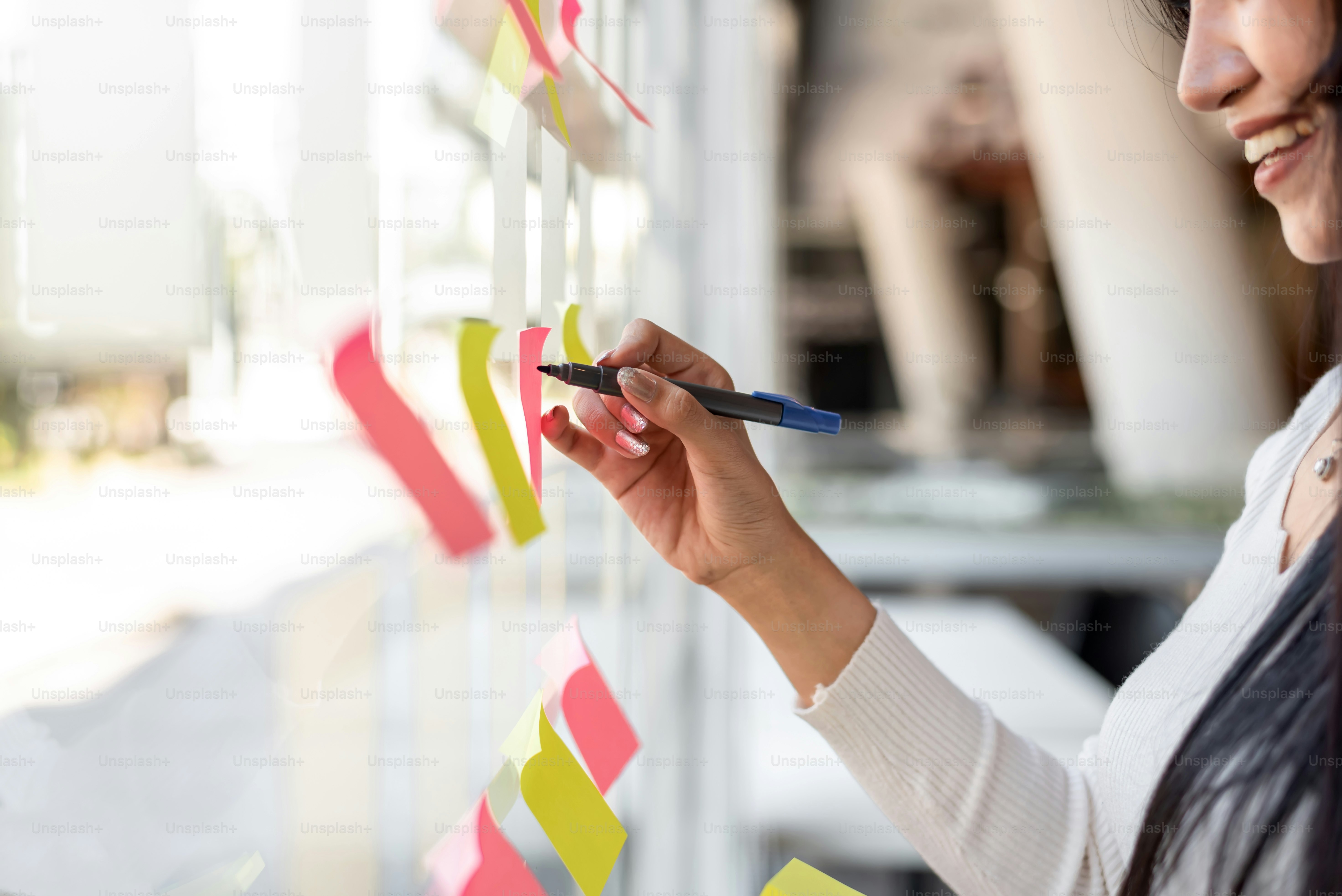 Close up hand businesswoman writing sticky notes on glass wall in office.