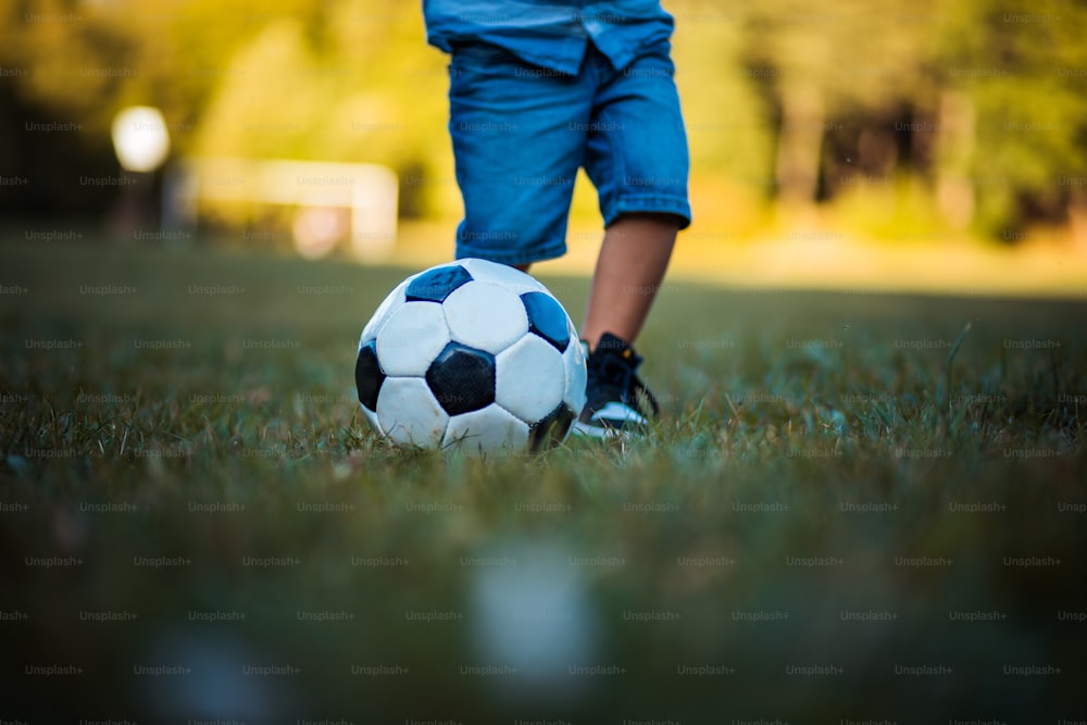 Piernas de niño pequeño jugando al fútbol en la hierba. Cerrar.