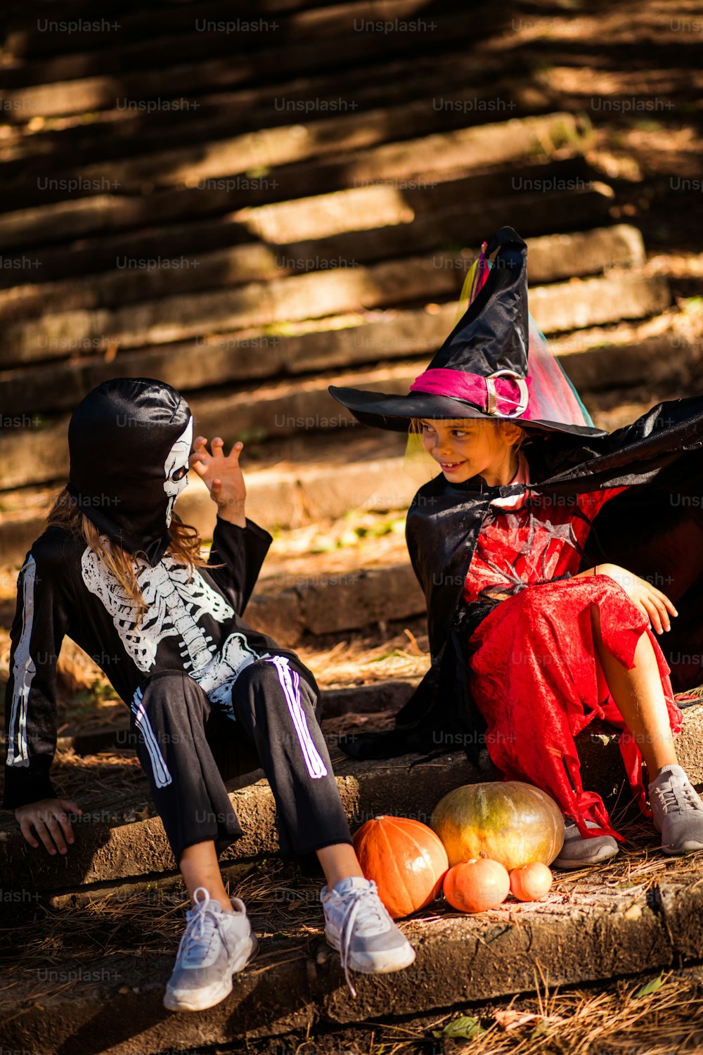 Conversa e diversão.  Duas meninas sentadas no parque. Crianças vestindo ternos de Halloween.