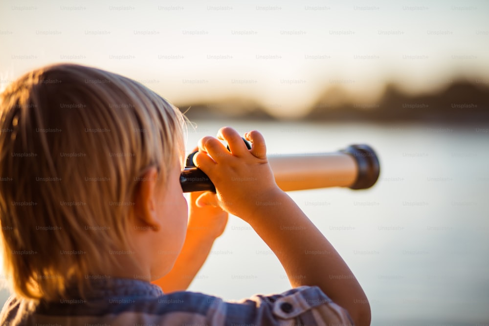 Little boy looking through telescope outside.