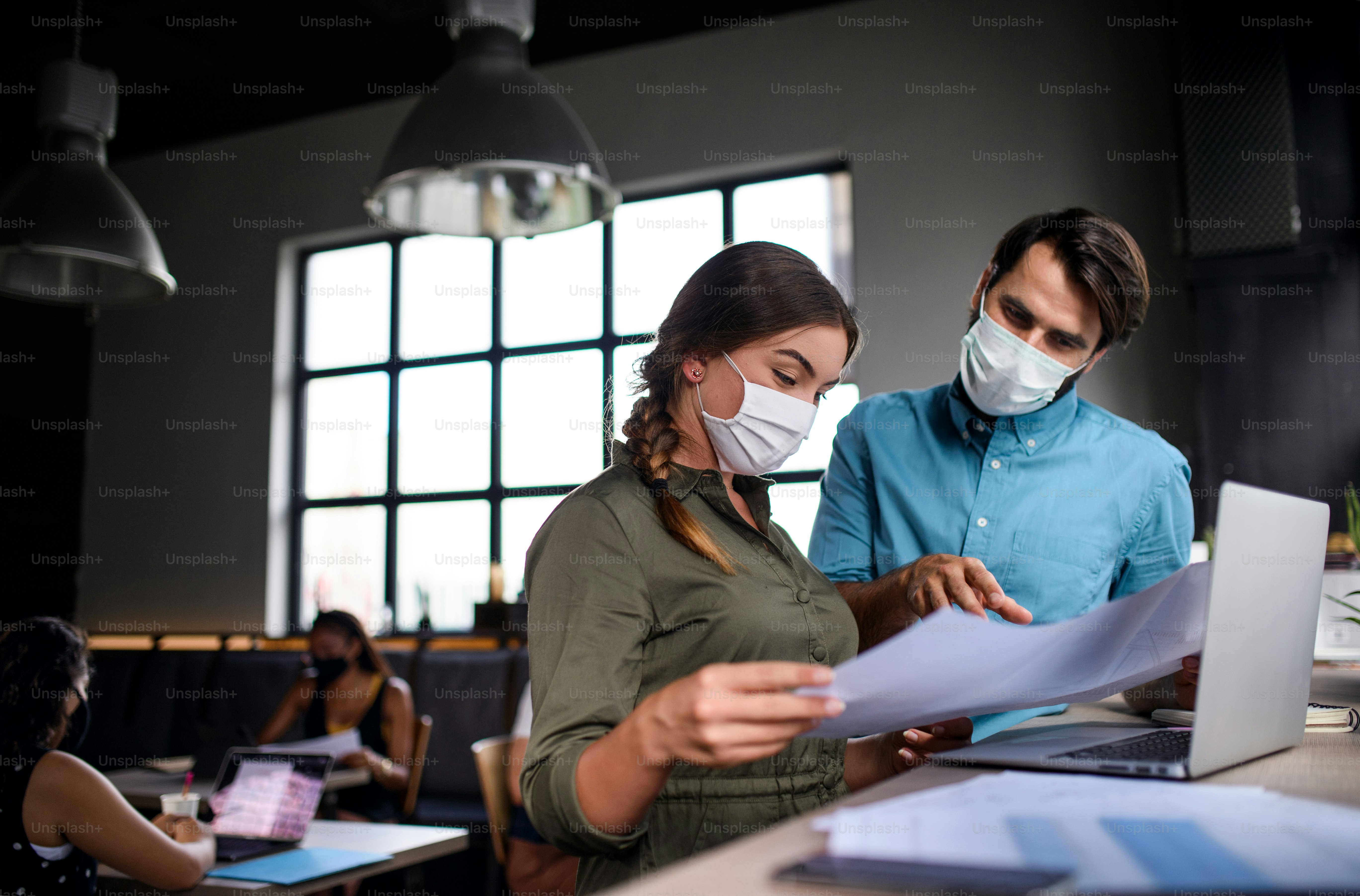 Business people with face masks working indoors in office, back to work after coronavirus lockdown.
