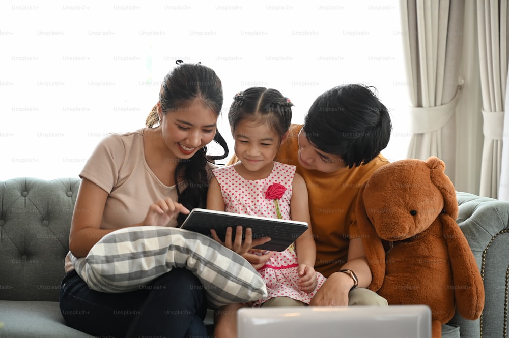 Familia joven casual con tableta digital navegando por Internet mientras elige películas o dibujos animados para ver en su tiempo libre.