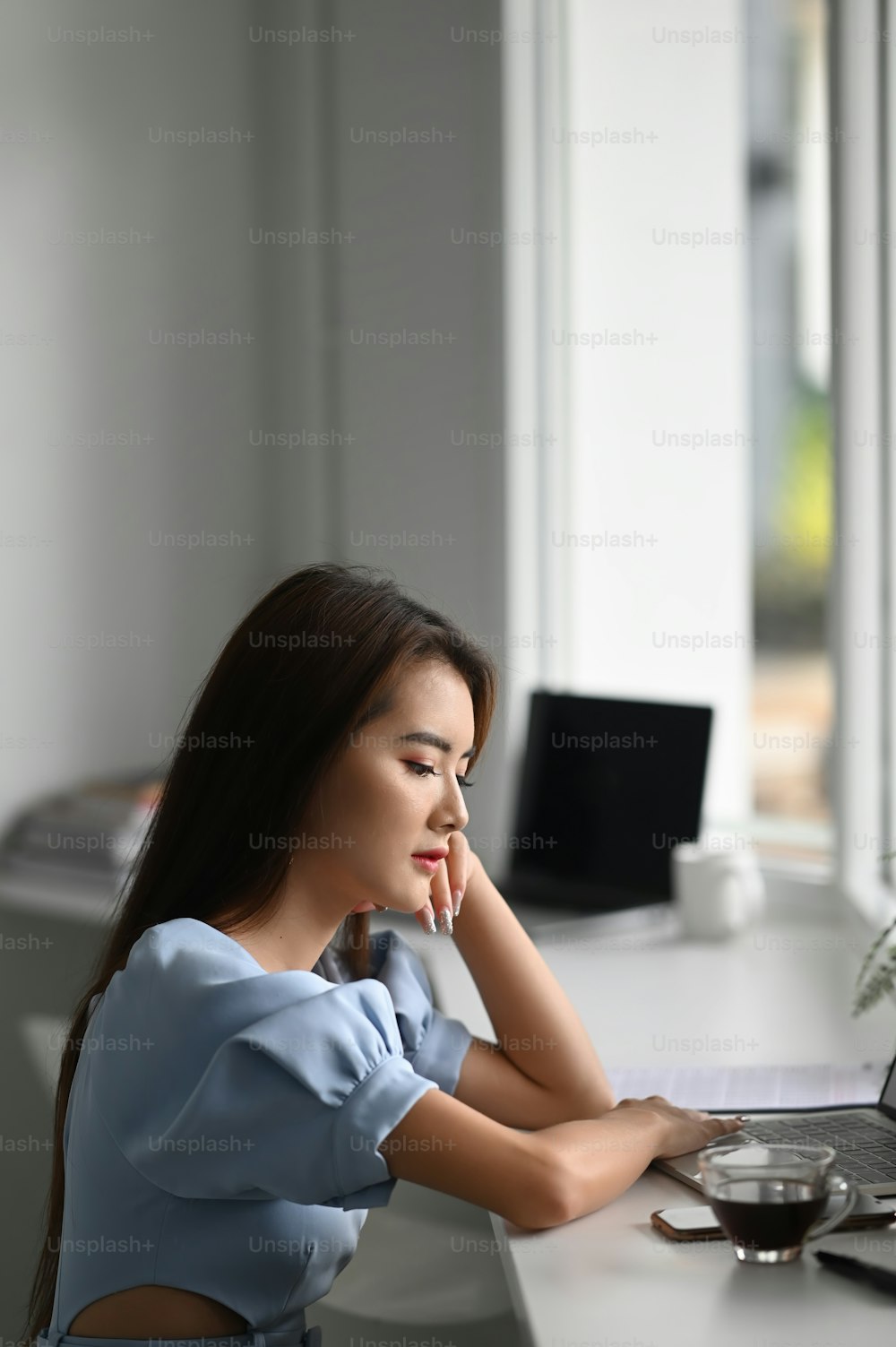 Porträt einer Freiberuflerin, die in ihrem Büro sitzt und auf den Bildschirm des Laptops schaut.