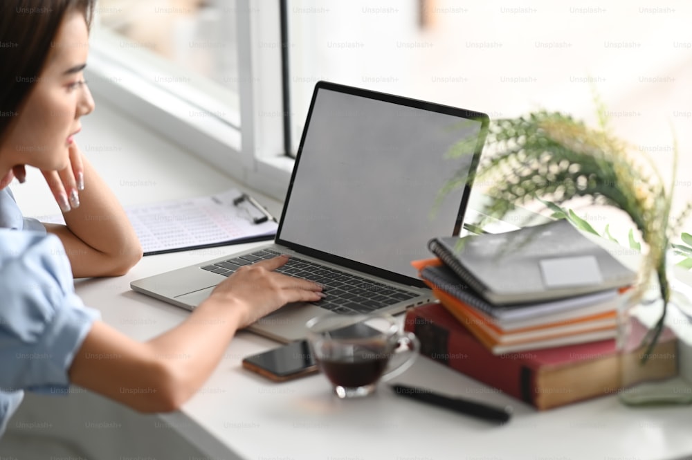 Ausschnittaufnahme einer jungen Frau, die ihr Projekt auf einem Laptop mit weißem Bildschirm im Büro plant.