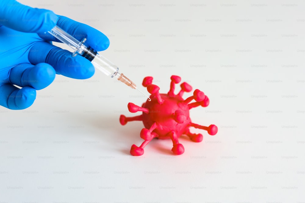 La persona sostiene una jeringa con la vacuna y le da una inyección a un virus corona rojo sobre el fondo blanco. Trabajador de la salud inyectando una vacuna en un patógeno como virus y bacterias