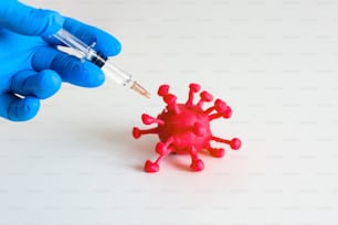 La persona sostiene una jeringa con la vacuna y le da una inyección a un virus corona rojo sobre el fondo blanco. Trabajador de la salud inyectando una vacuna en un patógeno como virus y bacterias