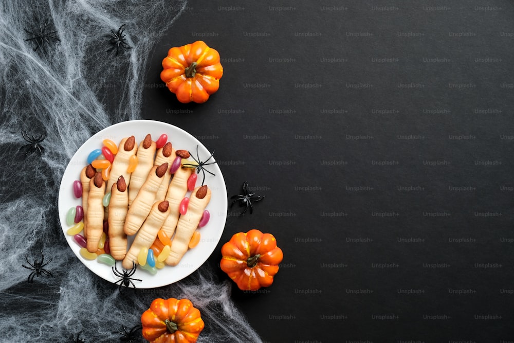 Halloween cookies in form of witches hand fingers, pumpkins, spiderweb on black background. Halloween banner mockup.