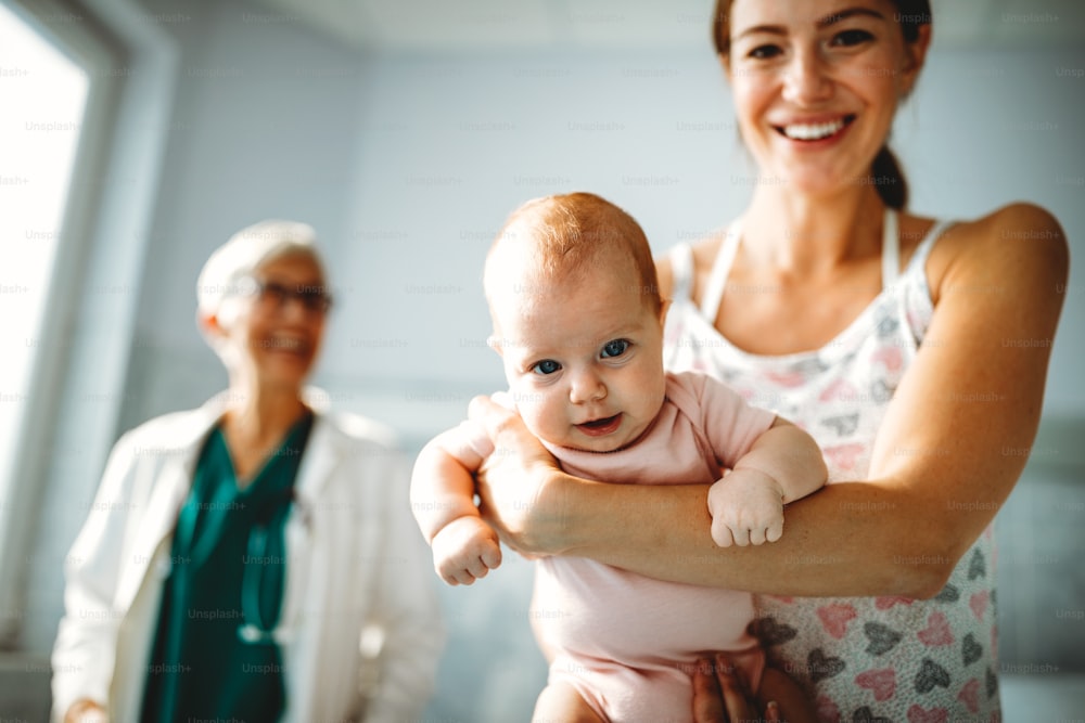병원에서 검사를 받는 행복한 엄마와 아기와 함께 있는 소아과 의사. 히스케어, 가족, 의사 개념.