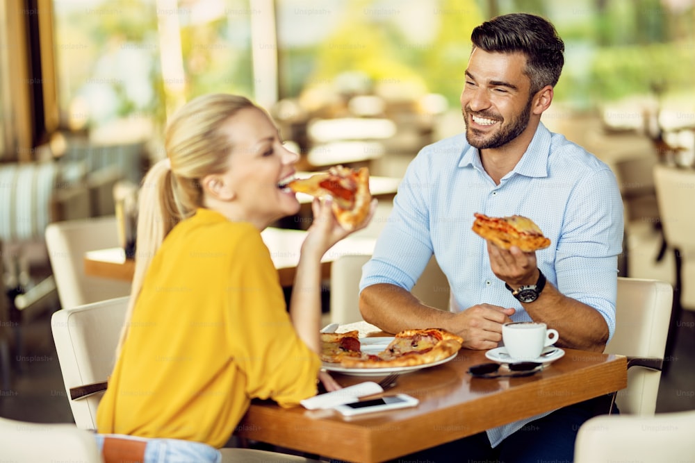 Happy couple having fun while eating pizza in a restaurant. Focus is on man.