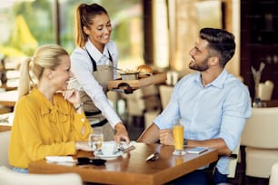 Jeune serveuse heureuse servant un repas à son invité dans un restaurant.