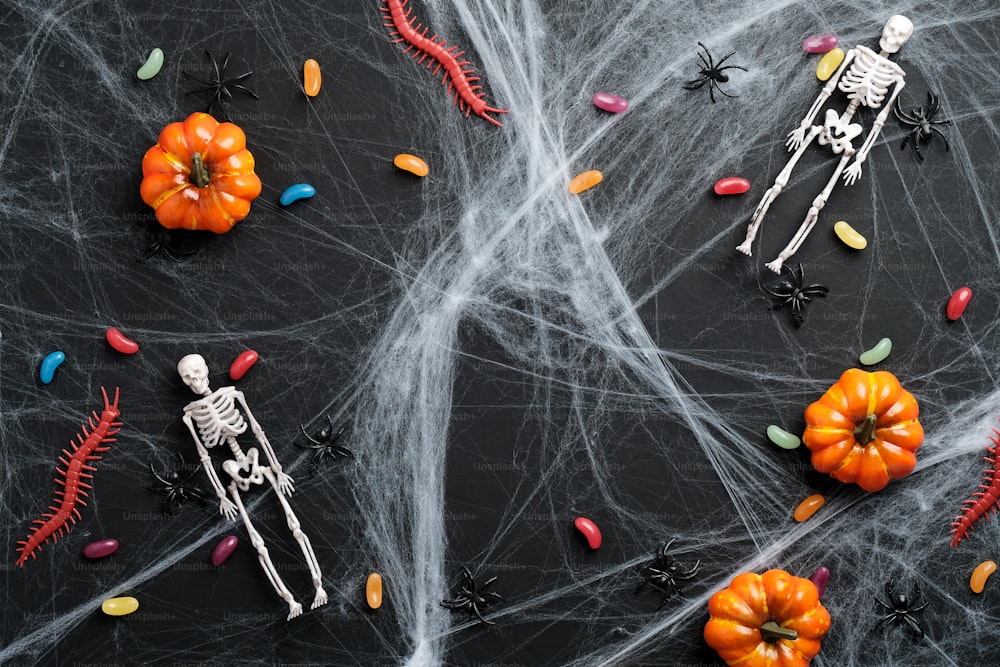 Sfondo nero di halloween con ragnatela, caramelle colorate, zucche, scheletri. Posa piatta, vista dall'alto. Buon concetto di Halloween.