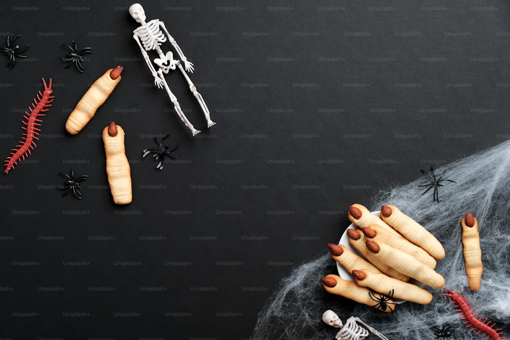 Galletas de dedos de Halloween, telaraña, esqueletos sobre fondo negro. Concepto de celebración de vacaciones de Halloween. Plano, vista superior, cenital.