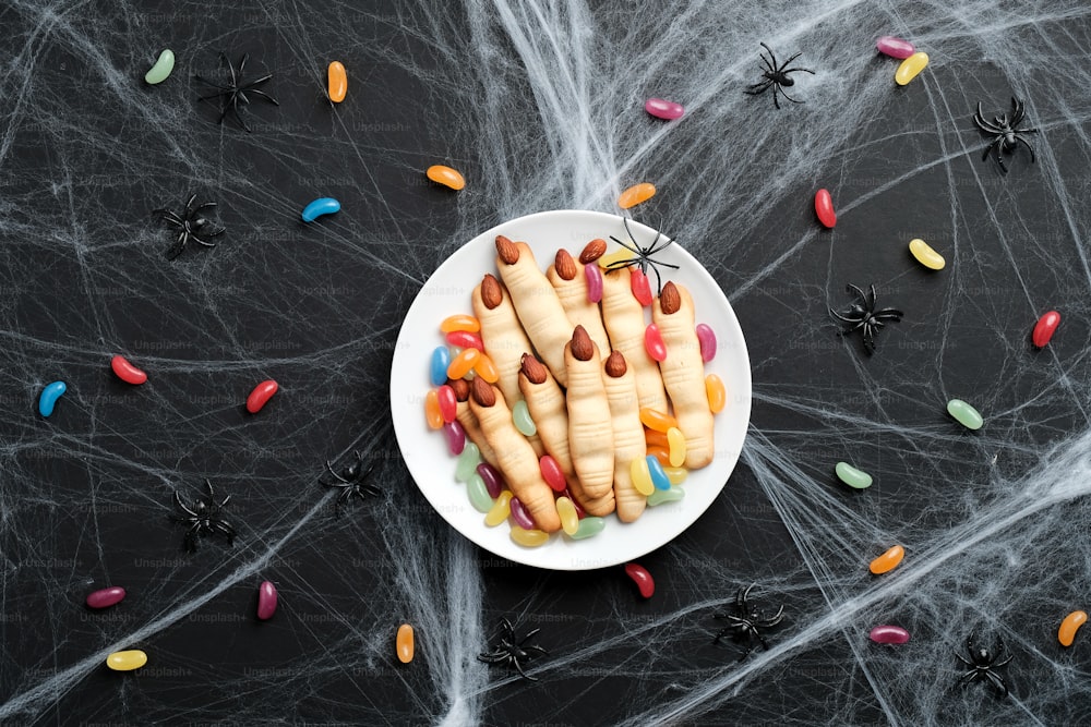 Halloween finger cookies with candies and spider webs on black background. Halloween food concept.