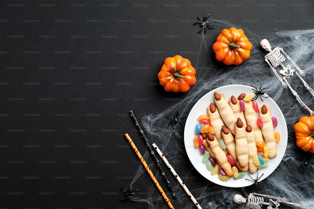 Halloween pastry concept. Halloween cookie in shape of witch fingers with almonds nails, pumpkins, spider webs, skeletons on black background