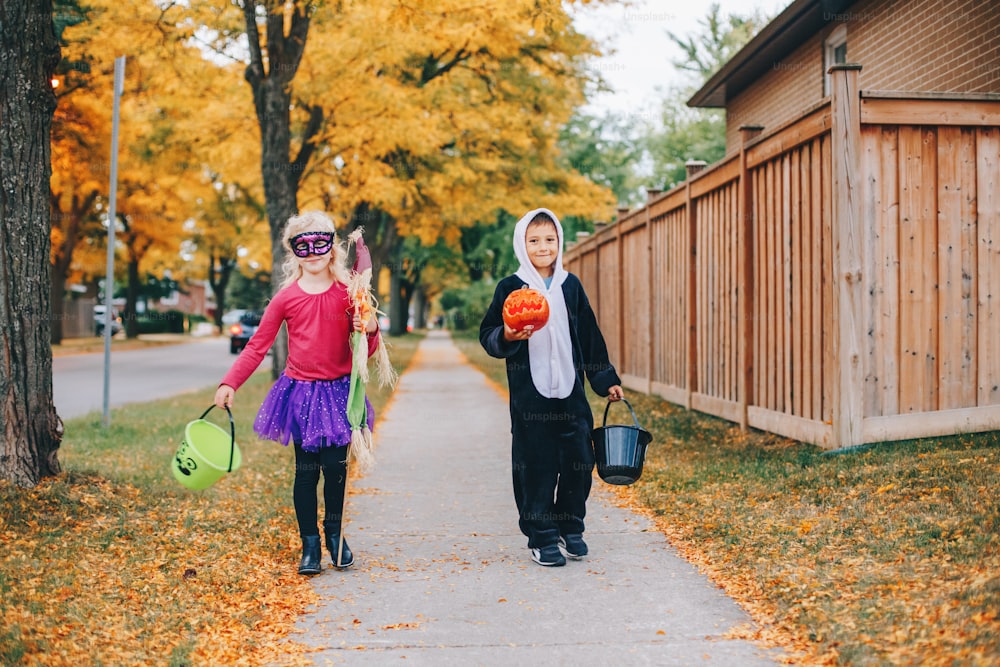Trick or treat. Happy children going to trick or treat on Halloween holiday. Kids boy and girl in party costumes with baskets going to neighbour houses for candies and treats.