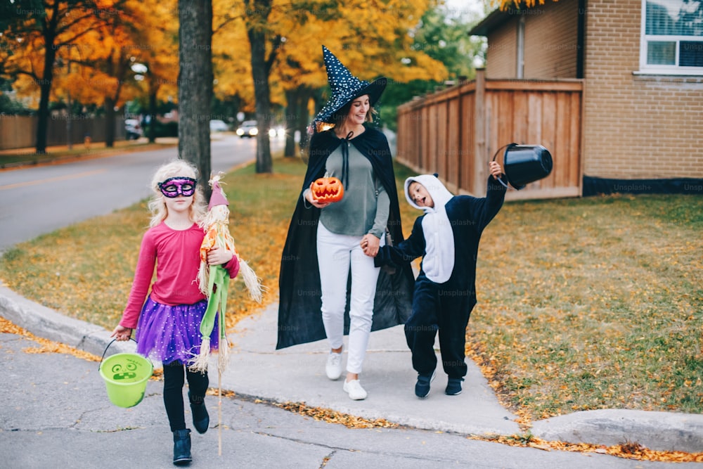 Trick or treat. Mother with children going to trick or treat on Halloween holiday. Mom with kids boy and girl in party costumes with baskets going to neighbour houses for candies and treats.