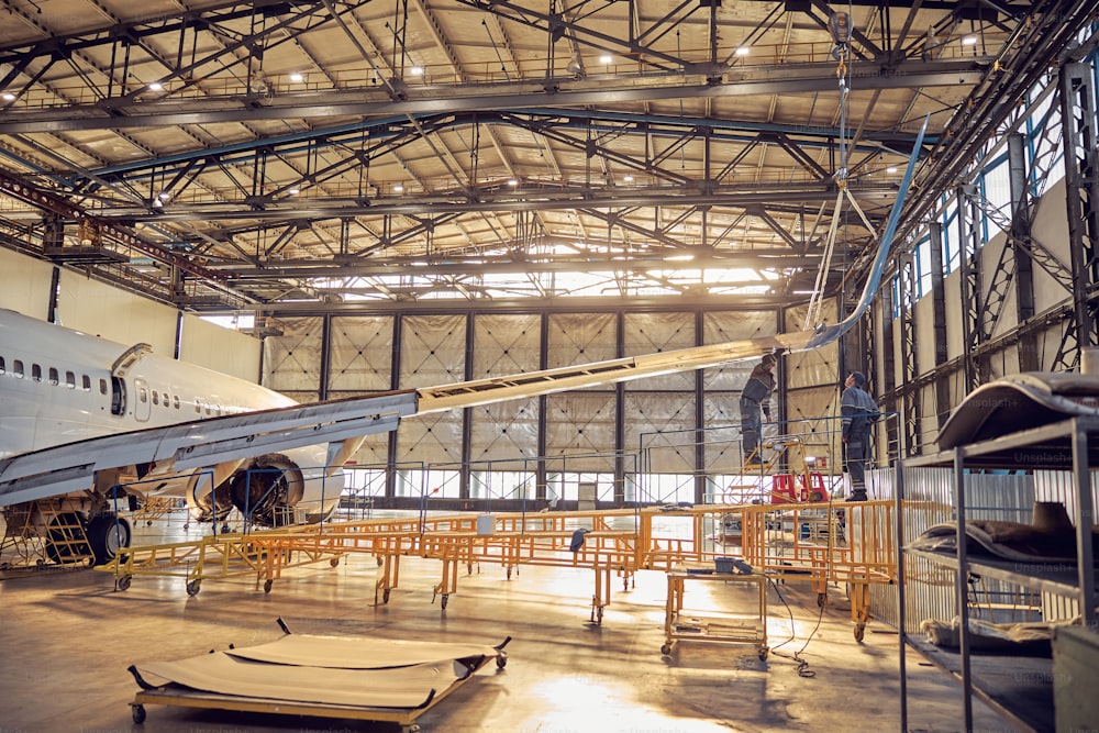 Full length portrait of aircraft engineers standing under wing with jet engine in aircraft maintenance factory