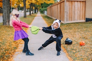 Wütende verrückte Kinder, die um den Korb kämpfen. Lustiges Süßes oder Saures am Halloween-Feiertag. Kinder Junge und Freundinnen in Partykostümen können keine Urlaubssüßigkeiten und Leckereien teilen. Geschwister familiäre Beziehung.