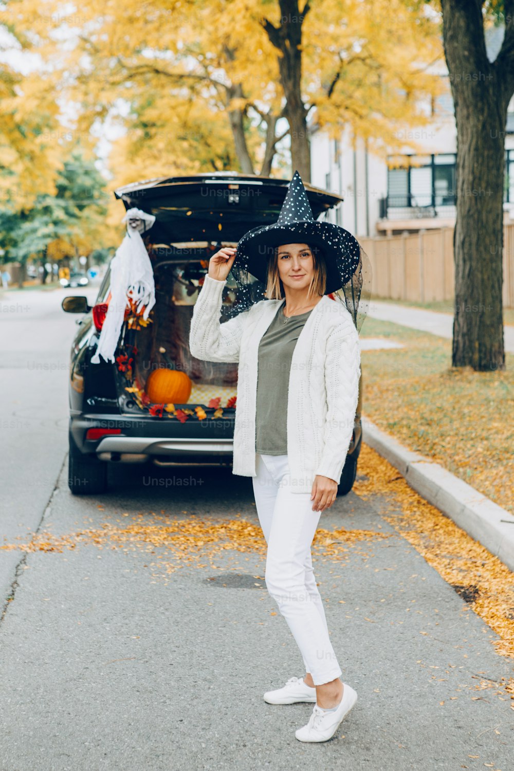 Trick or trunk. Woman in witch hat celebrating Halloween in trunk of car. Mother preparing for celebrating traditional October holiday outdoor. Social distance and safe alternative celebration.