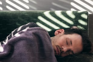 A caucasian man taking an afternoon nap on couch at home with shadow of blinds