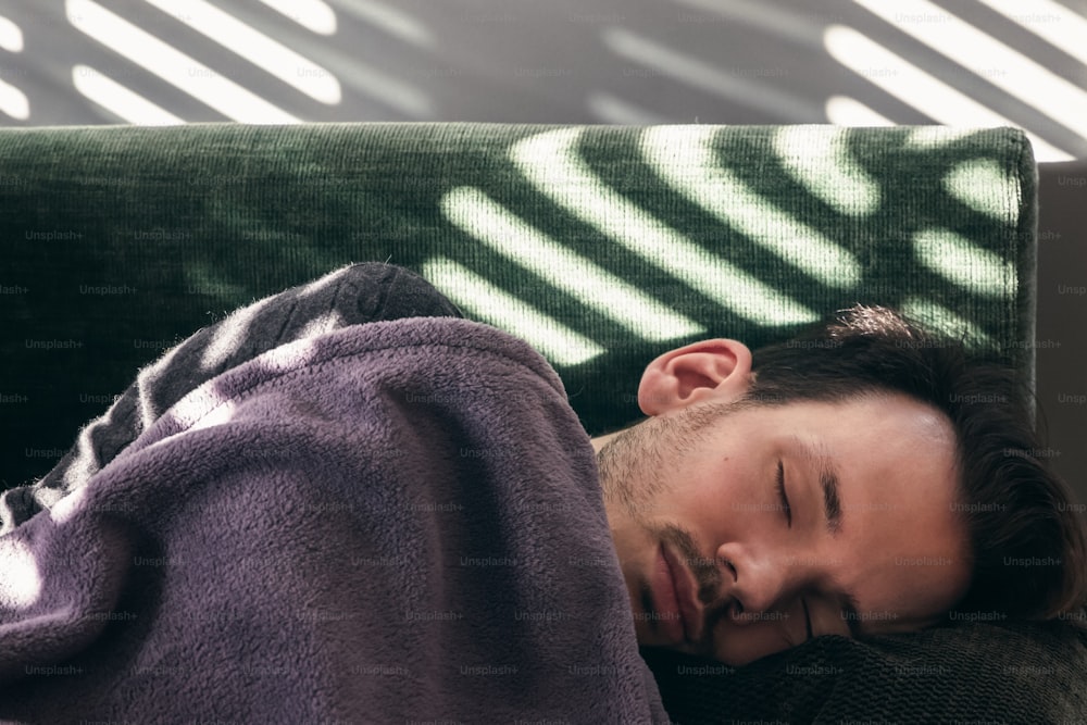 Un hombre caucásico tomando una siesta por la tarde en el sofá de su casa con la sombra de las persianas