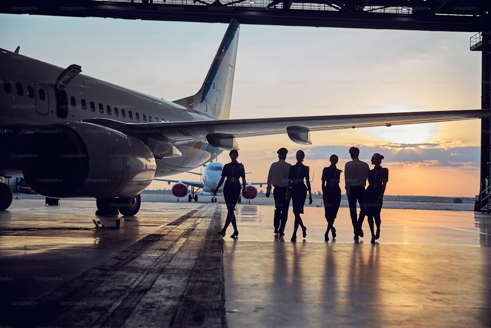 Imagem do grande avião de passageiros em pé no hangar do aeroporto enquanto a equipe voadora passa o tempo perto dele