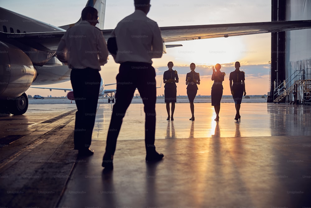 Back view portrait of flight staff standing in the aviation hangar in the evening at the sunset